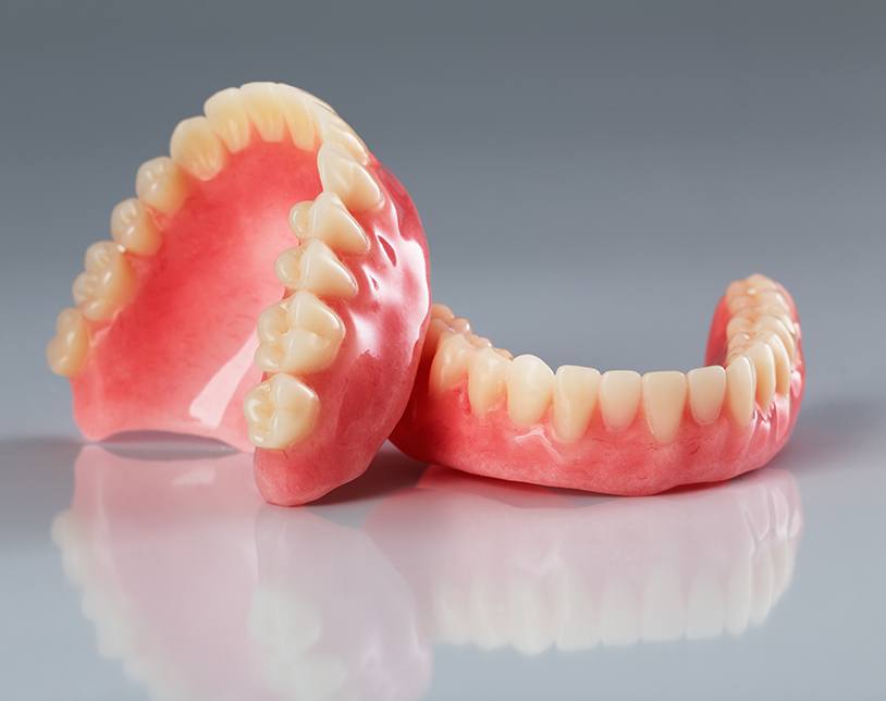 Full set of upper dentures resting on lower ones on a reflective gray surface