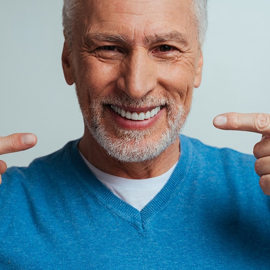 Older man in blue shirt pointing to his smile with both pointer fingers