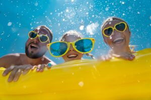 Man, girl, and woman in yellow glasses on a yellow floaty in laughing in the sun